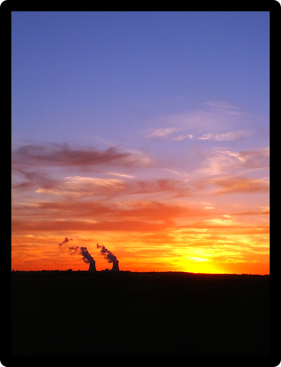 Bright sunset over two giant cooling towers at a nuclear plant.