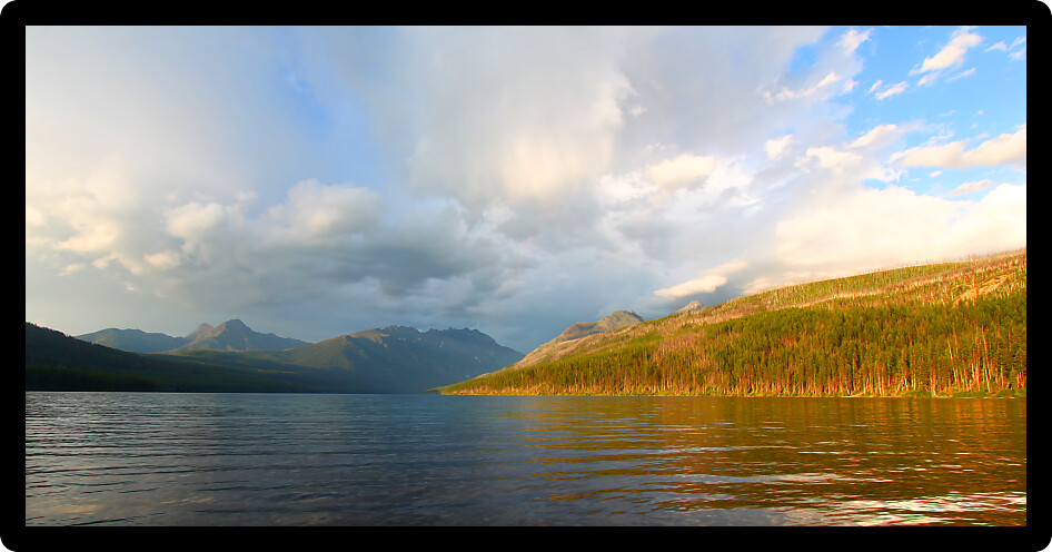 Sunlight illuminates the shoreline of Kintla Lake against a stormy sky in Glacier National Park - USA.