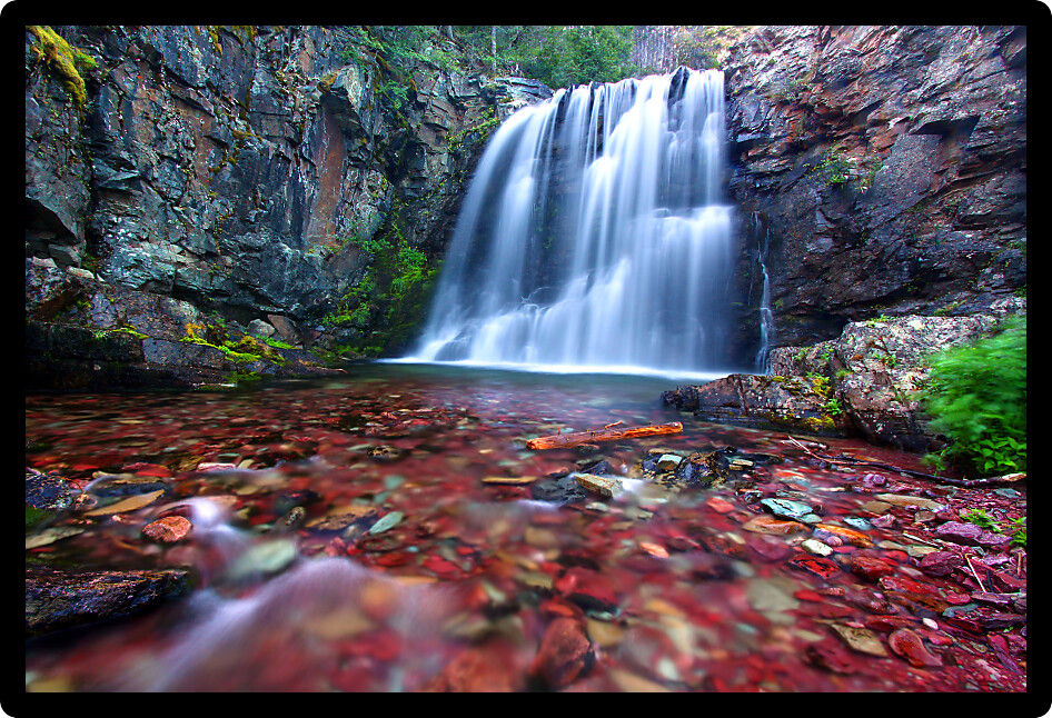 Bright stones shine through clear waters of Rockwell Falls in Glacier National Park.