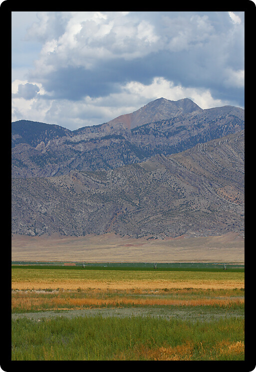 Mountains rise tall beyond a flat agricultural valley of Idaho.